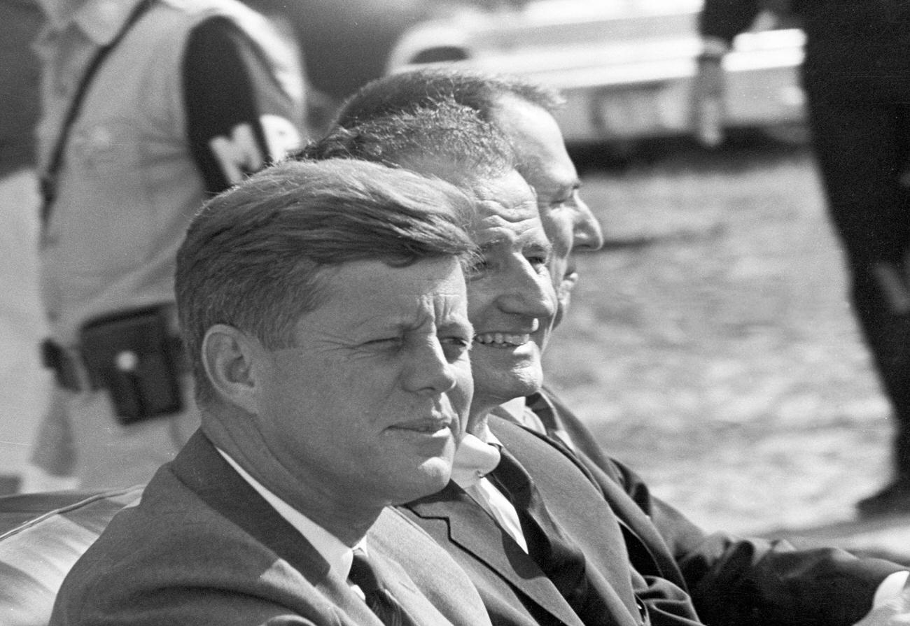 John F. Kennedy rides with others in an open-top convertible during a motorcade in Tampa, Florida, 1963.