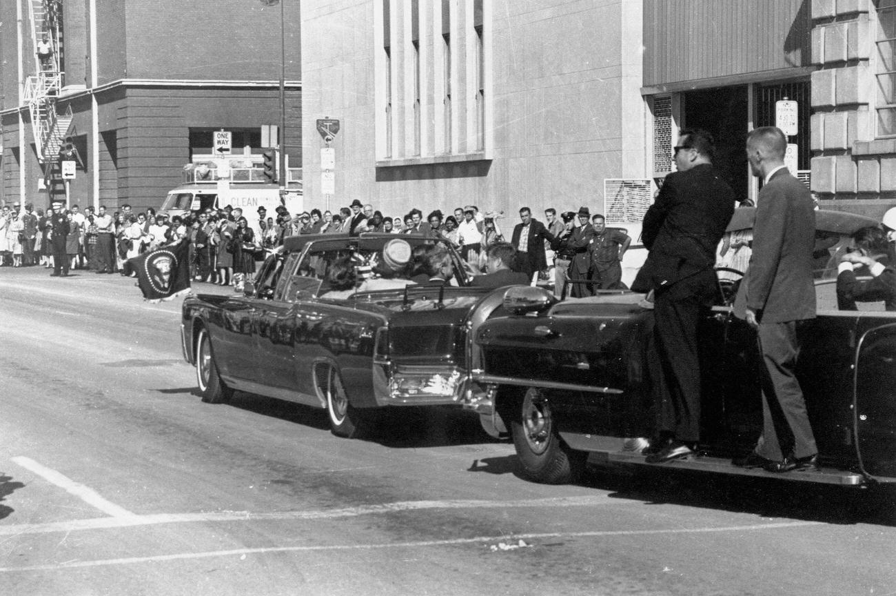 John F. Kennedy's motorcade passes the Texas School Book Depository in Dallas, Texas, before the assassination, 1963.