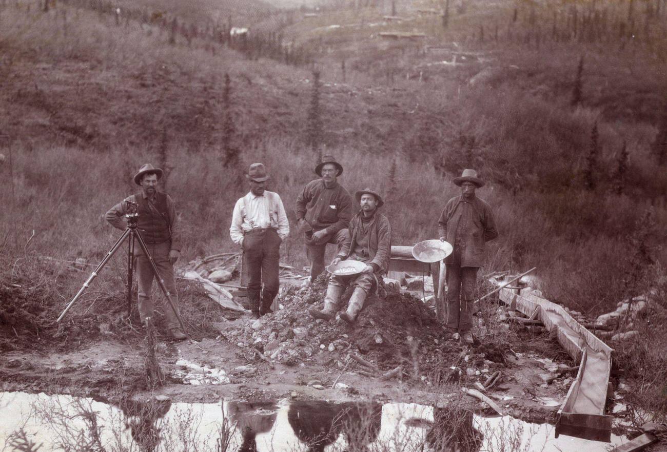 Men beside a stream with gold panning tools in Little Dominion during the Gold Rush.