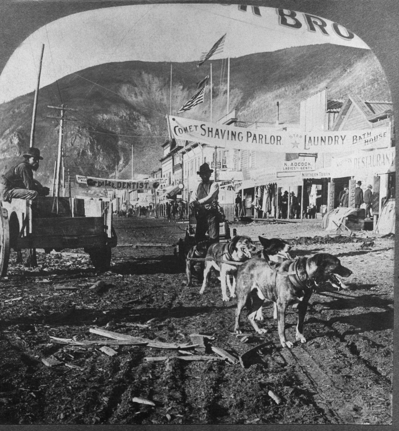 Dawson City, Alaska, street scene with carts, banners, pedestrians, and American flags during the Gold Rush, 1900.