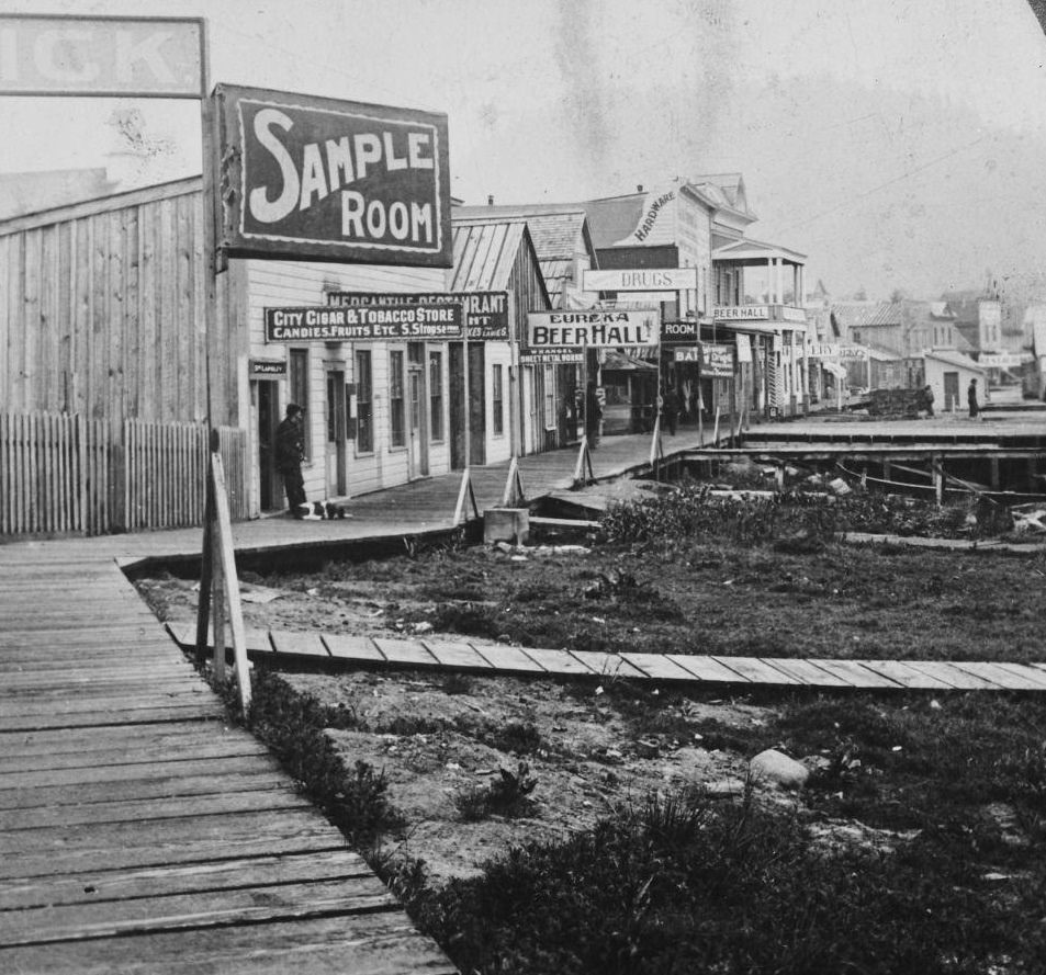 Main Street in Wrangell, Alaska, featuring saloons and totem poles, during the Klondike Gold Rush, circa 1900.