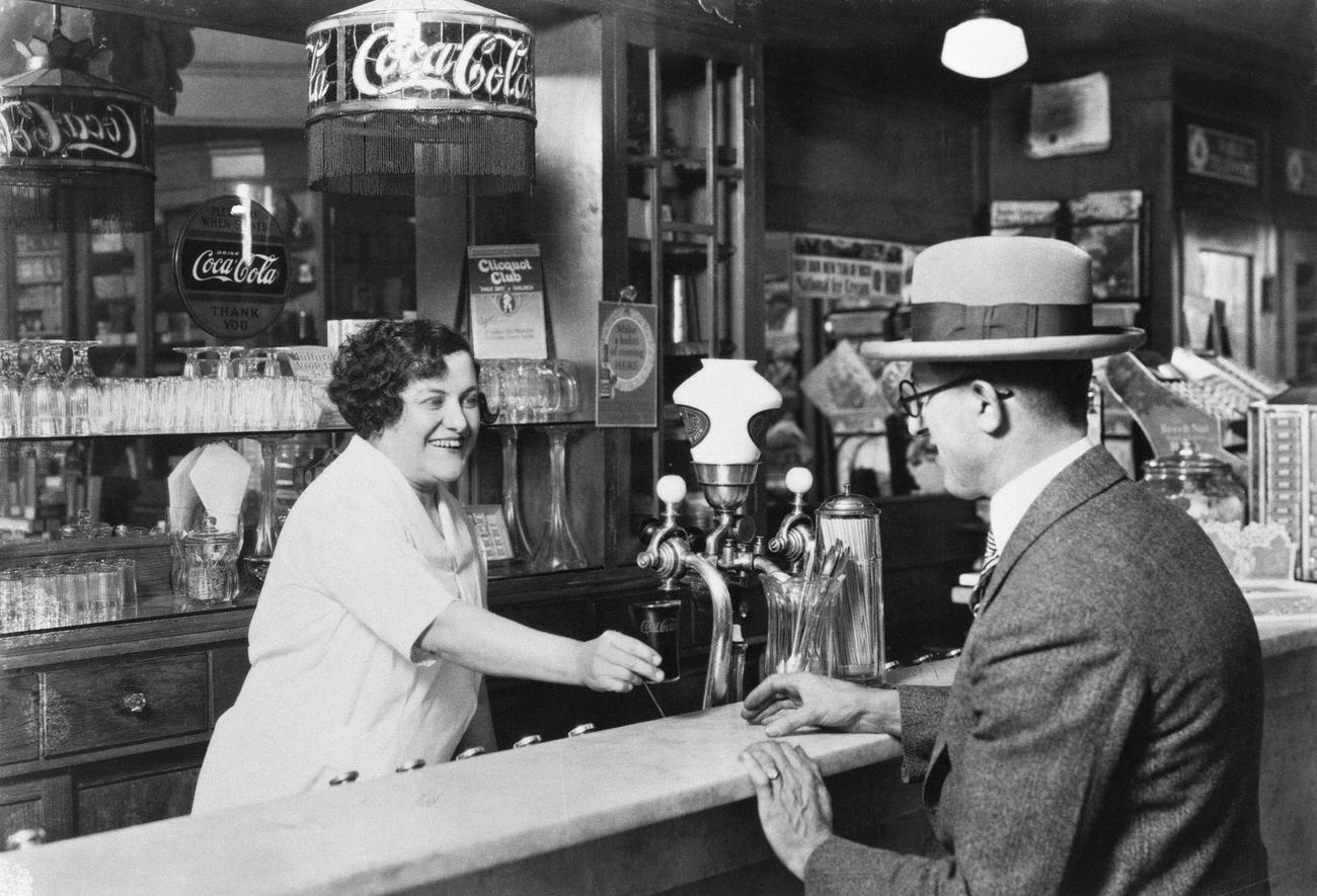 A counter girl serves Coca-Cola at a soda fountain, 1927.
