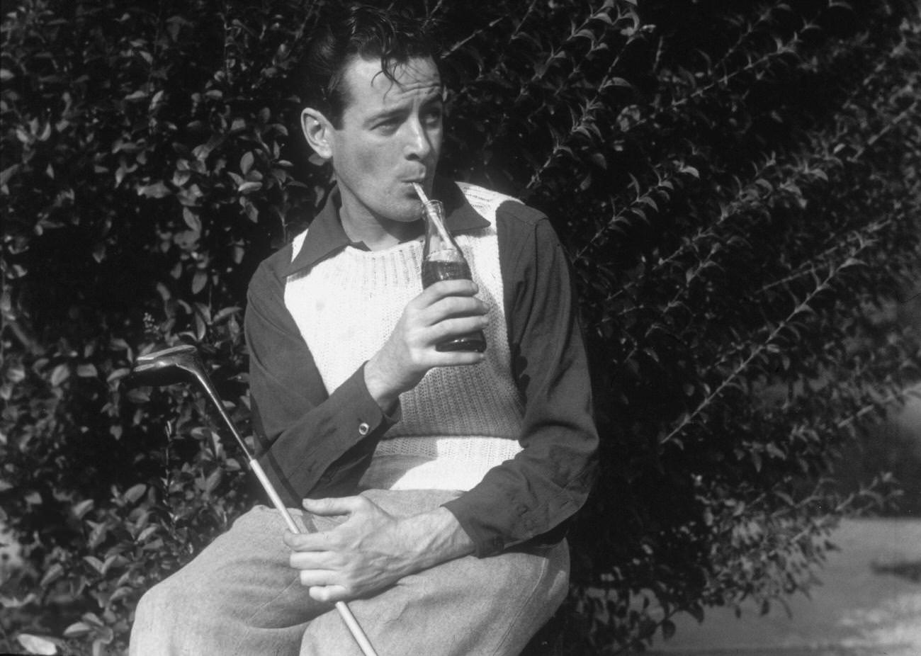 A young man sipping Coca-Cola with a golf club outdoors, circa 1935.