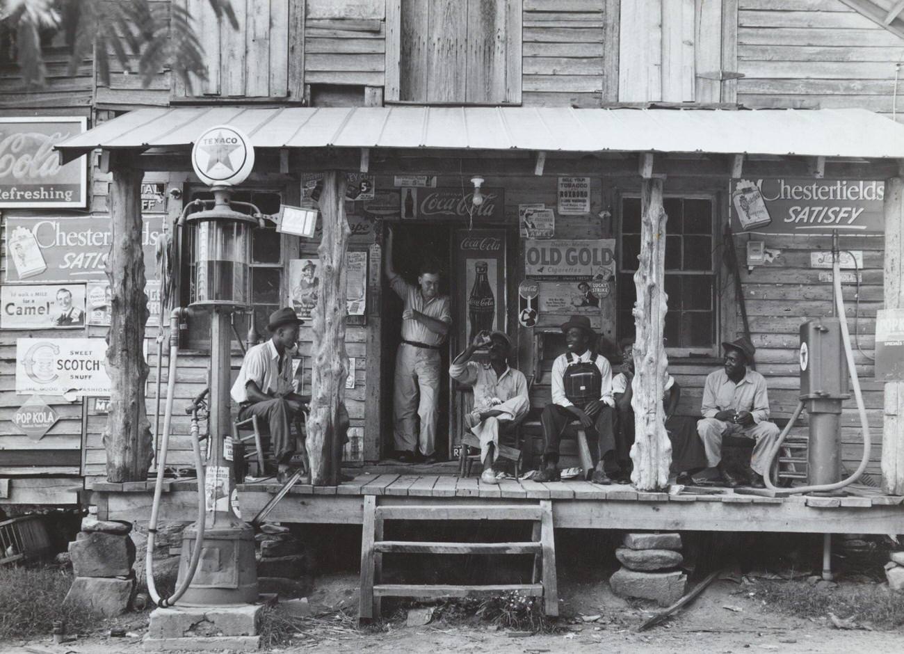 African American and a white store owner on the porch of a country store, circa 1939.