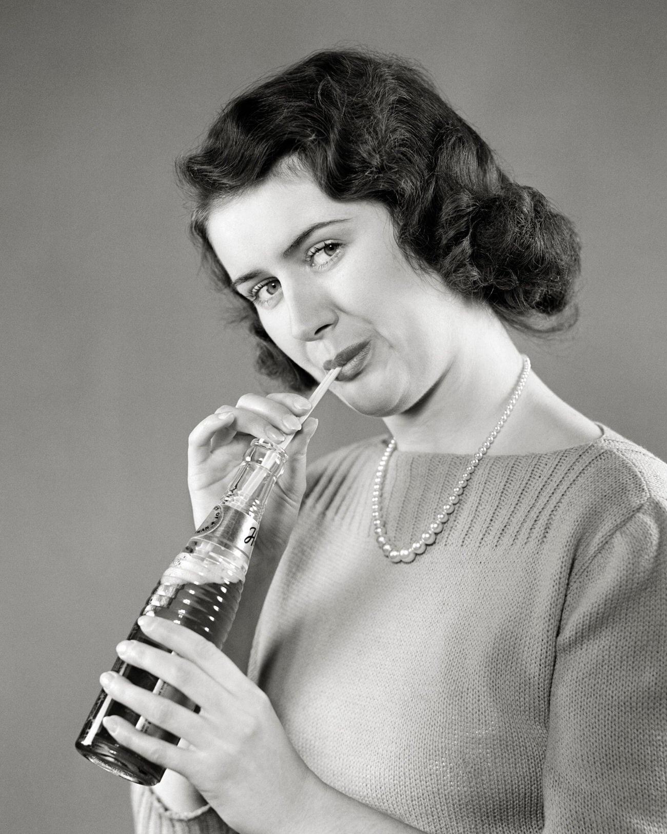 A smiling brunette woman holding a Coca-Cola bottle, 1940s.