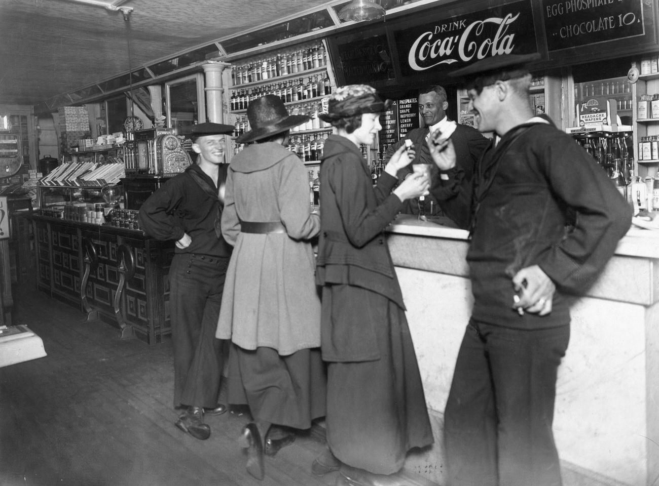 Two sailors and their dates drinking Coca-Cola at a soda fountain, World War I era.