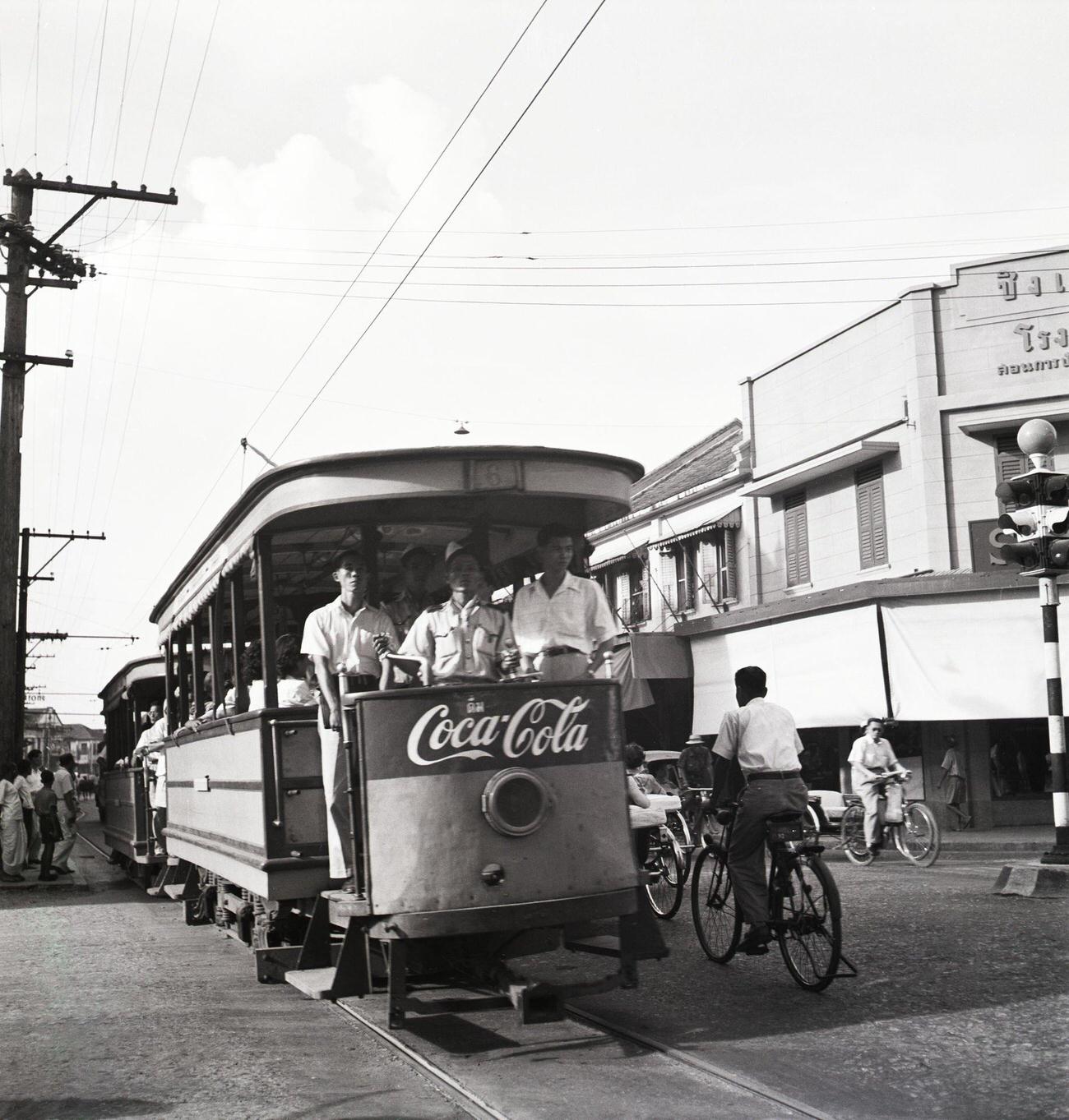 Cyclists pedaling by trolleys advertising an American soft drink in Siam, May 26, 1950.