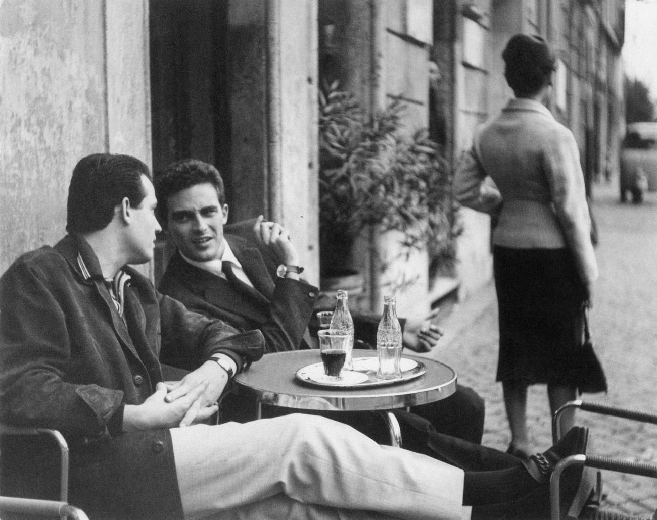 Two men chatting at a café table with Coca-Cola bottles, 1959.