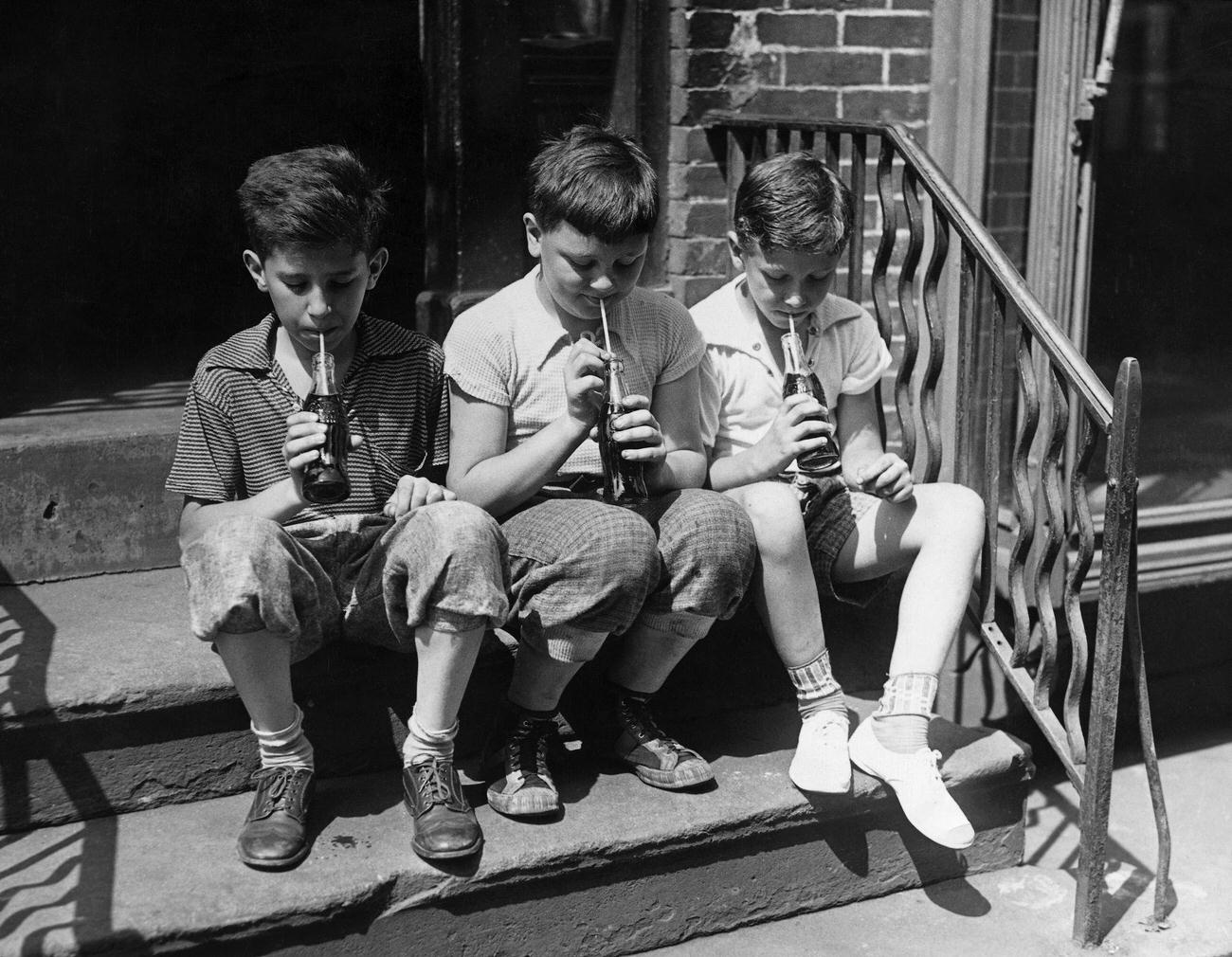 Three young boys cooling off with Coca-Cola on a stoop, undated.