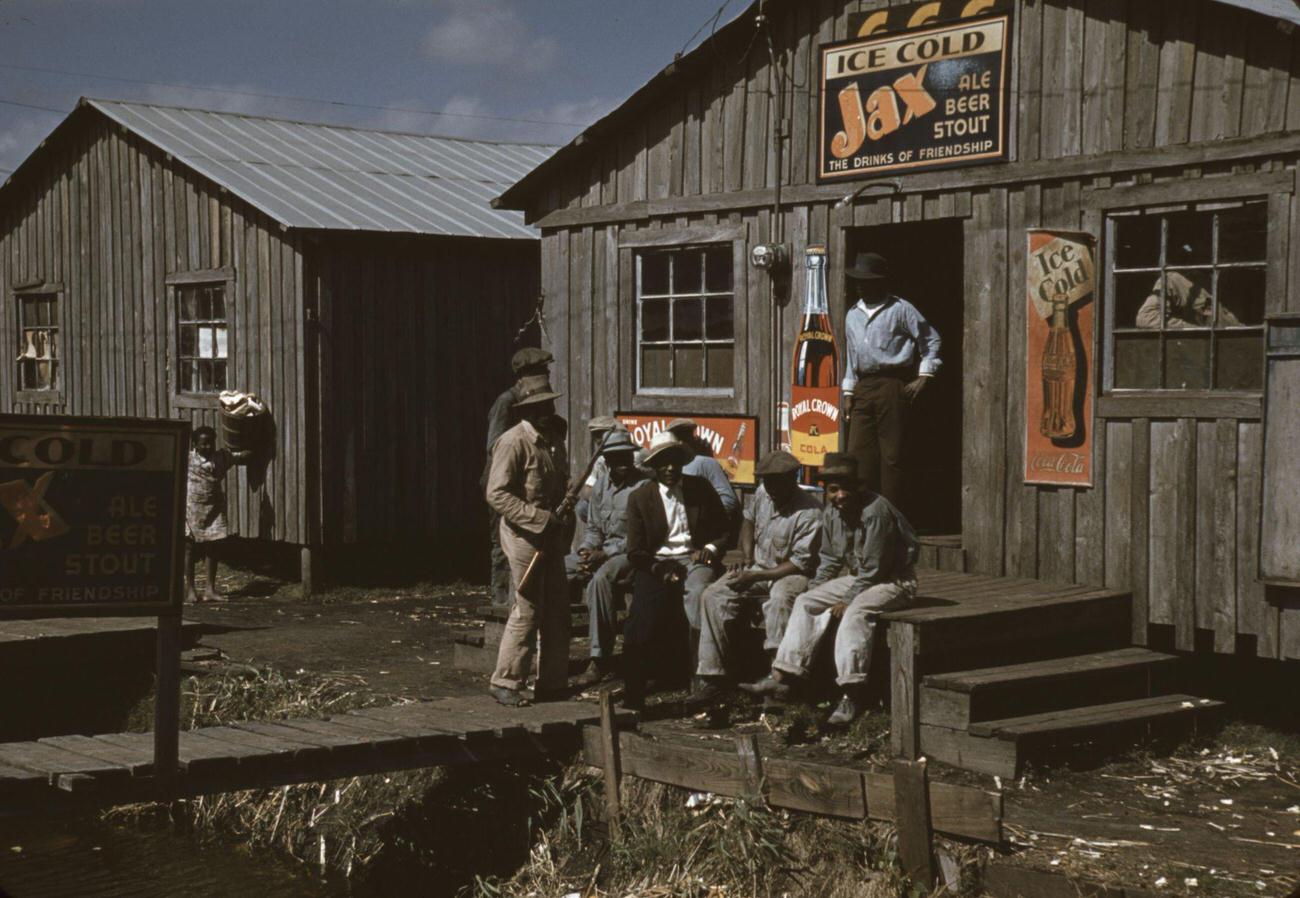Migratory laborers outside a "juke joint" in Belle Glade, Florida, with various beverage signs.