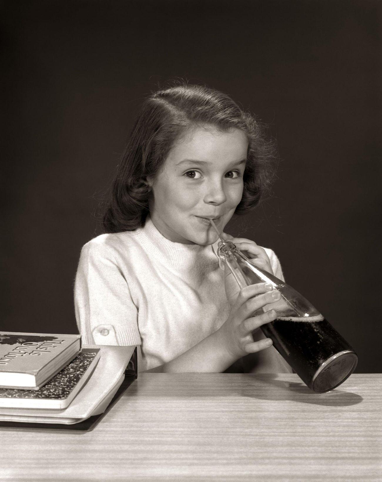 Smiling school girl drinking a carbonated beverage from a bottle, 1950s