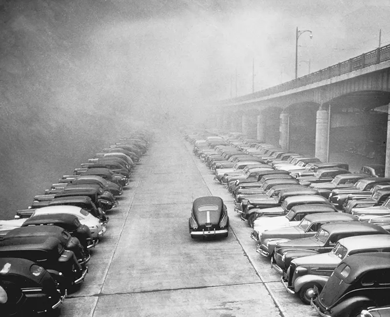 Cars parked on Monongahela Wharf under an overpass in smoke.