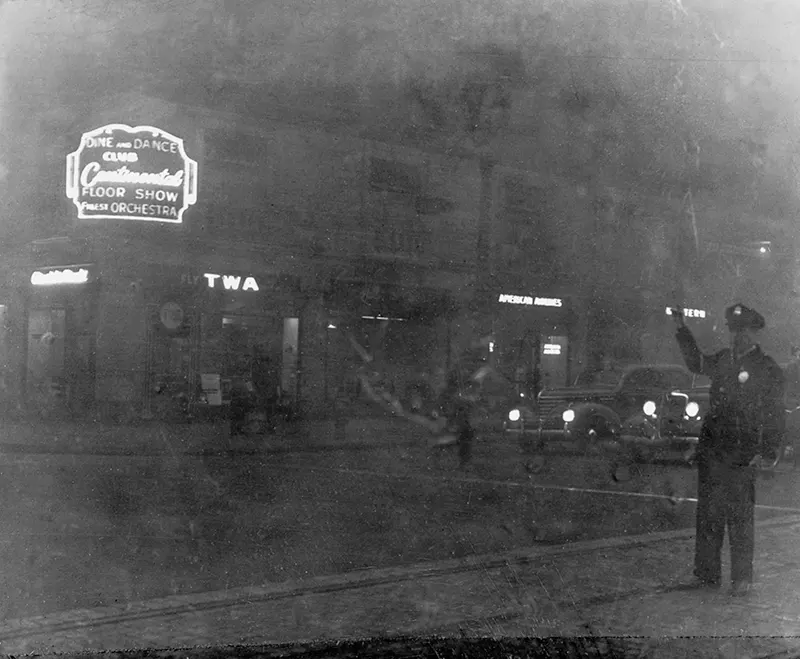 Saint Louis street before smoke ordinance, featuring various signs and a traffic-directing officer.