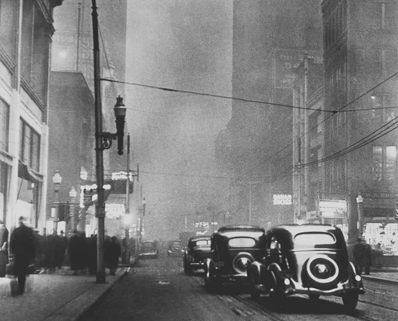 Pedestrians and tram lines in a smoky, dark midday street scene.