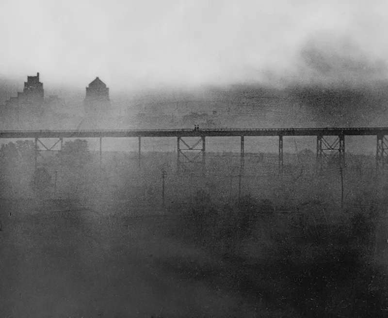 Dense smoke obscuring a bridge and distant buildings.