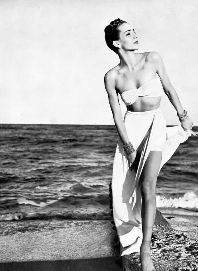 A model in a stone-white rayon-jersey two-piece swimsuit with a long evening skirt and Lampl jewelry, Harper's Bazaar, 1945.