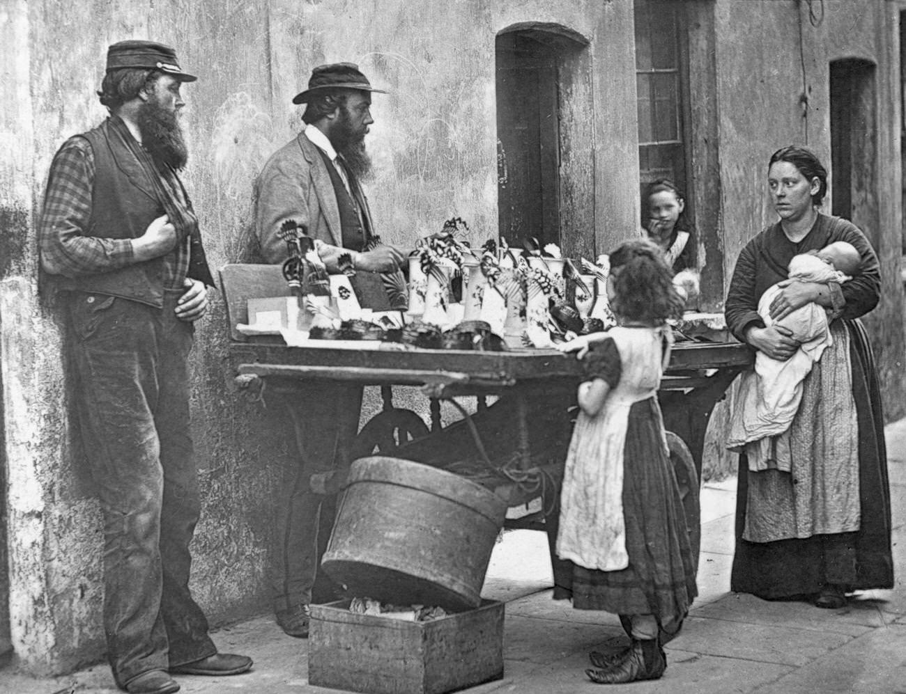 Victorian fancy wear dealer selling ornaments from his barrow, 1877.