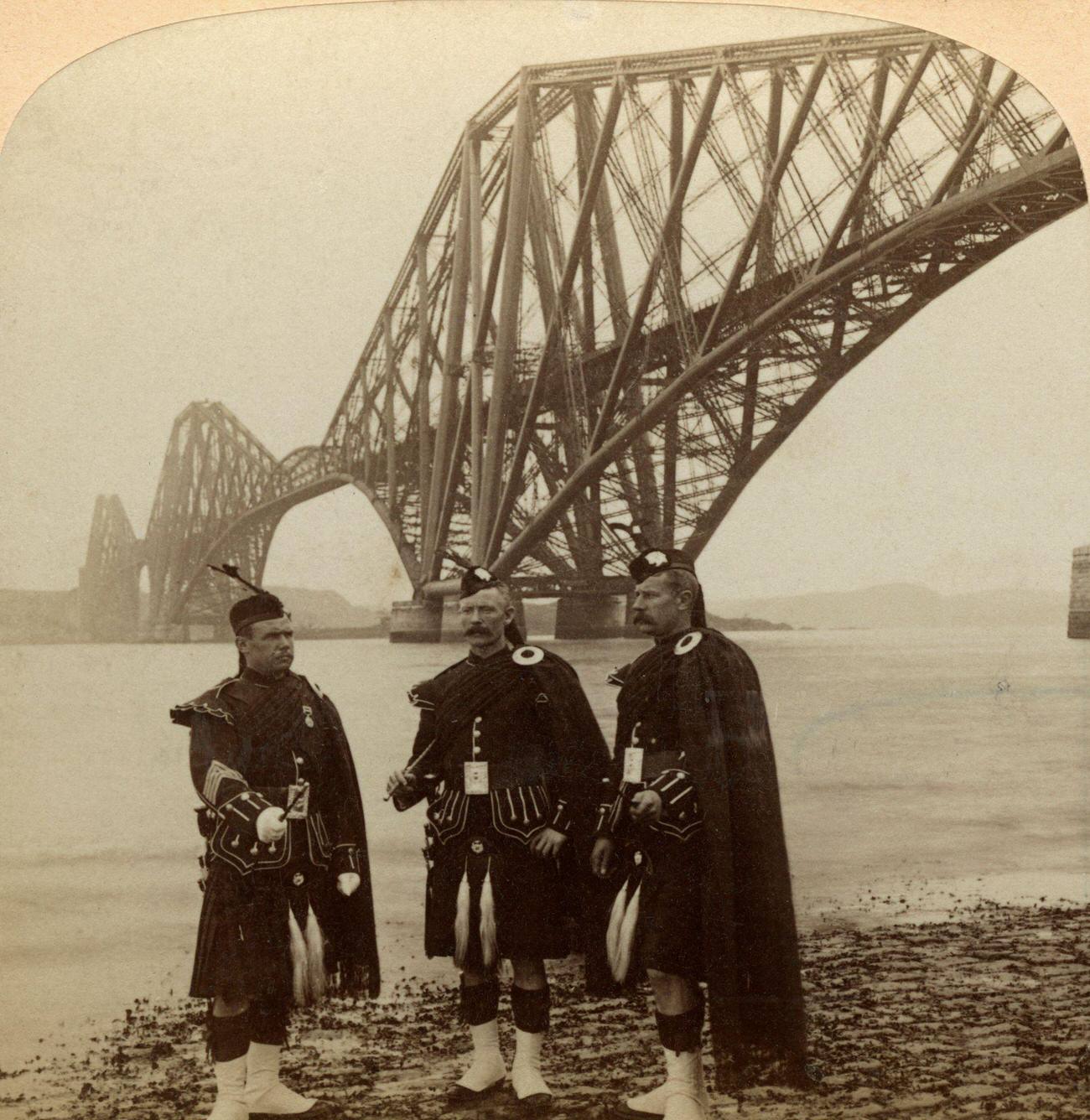 Men in Highland dress in front of the Forth Bridge, Scotland.