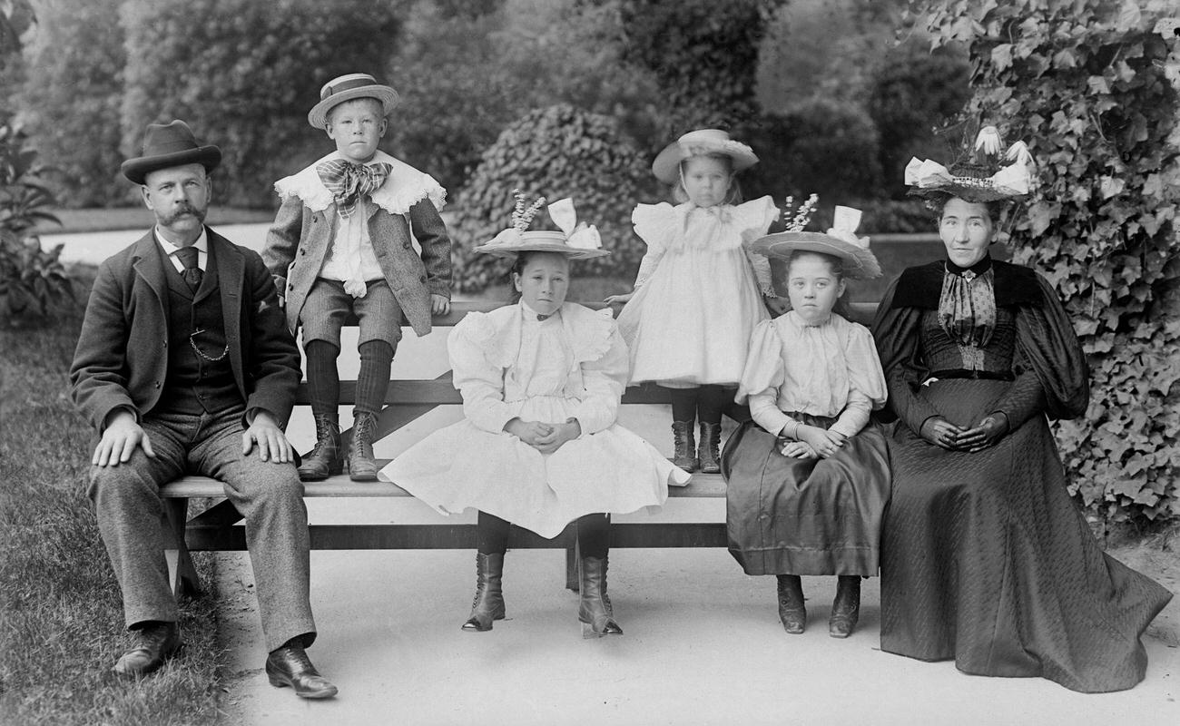 Family posing for a formal portrait on a garden bench, circa 1890.