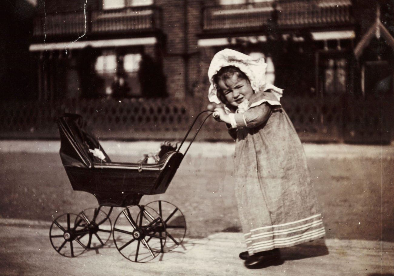 Child pushing a toy pram, circa 1895.