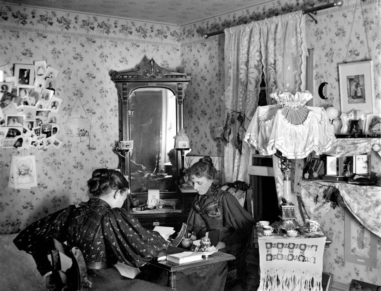 Two women at a writing desk in a Victorian parlor, circa 1898.