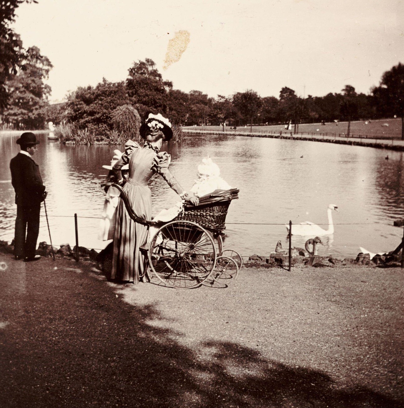Woman and wheelchair near a lake in a park, circa 1900.