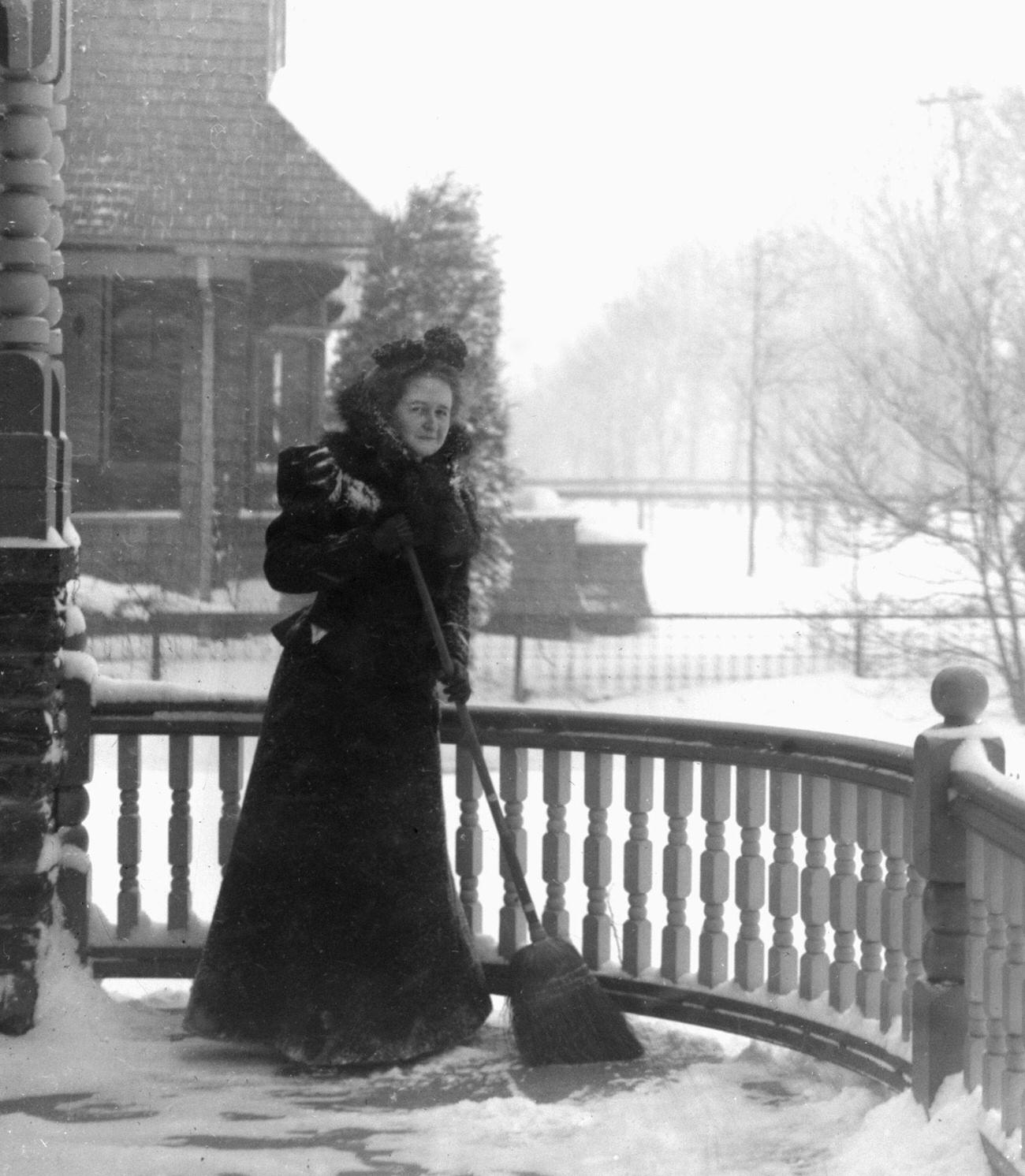 Victorian woman clearing snow off her porch, circa 1900.