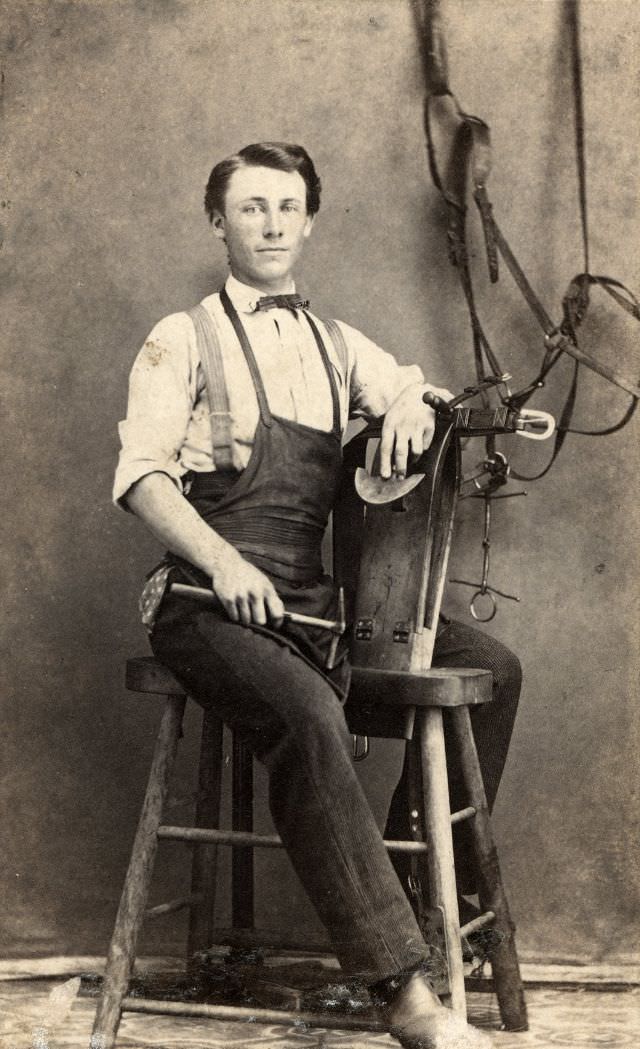 A harness maker poses with his tools of his trade with a bridle as a backdrop