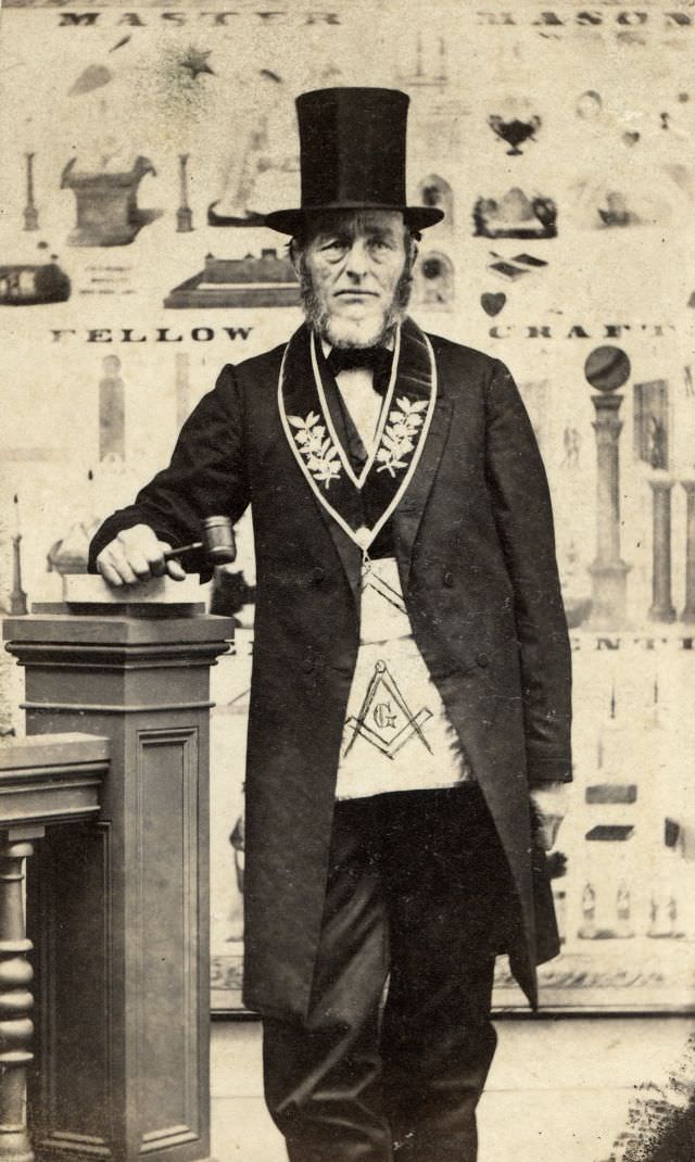 A Mason grasps his gavel in front of a backdrop customized for his fraternal organization. The gavel its one of the ancient symbols of Freemasonry