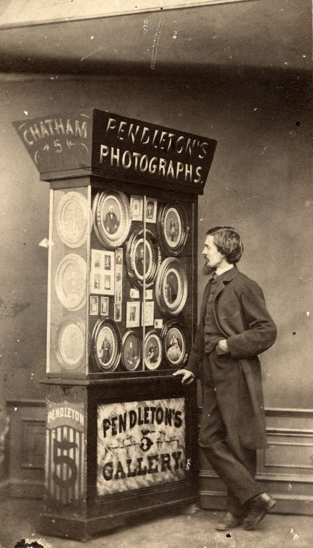 The man standing in front of a display cabinet full of photographic portraits is very likely the lensman who made them