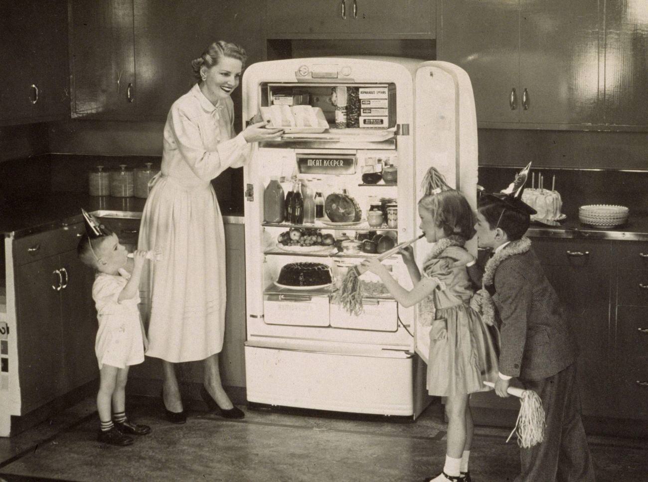 Woman and children with cake from refrigerator, circa 1948.