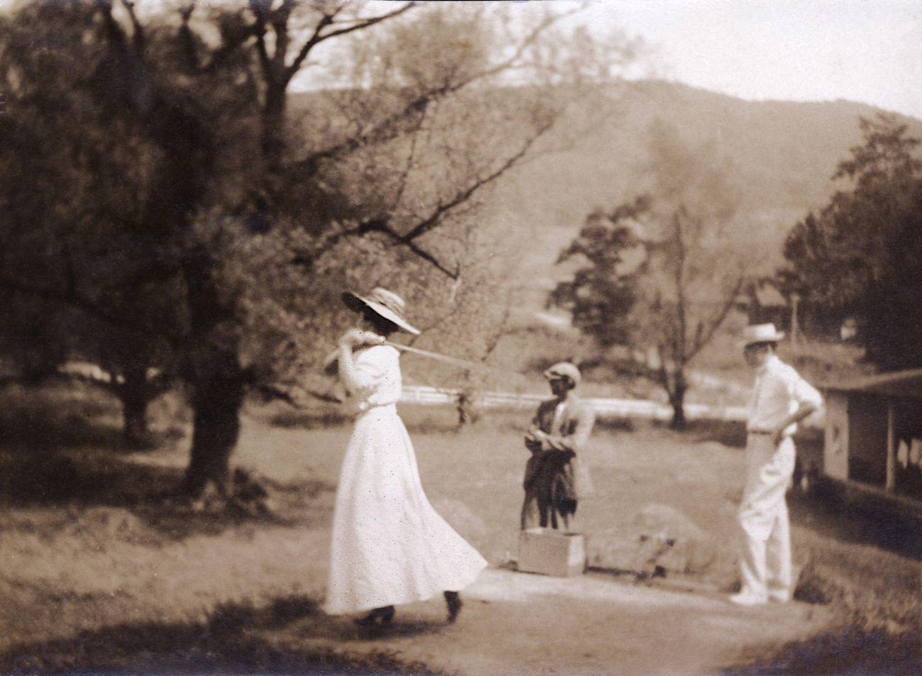 Early twentieth-century woman golfer with male companion and caddy.