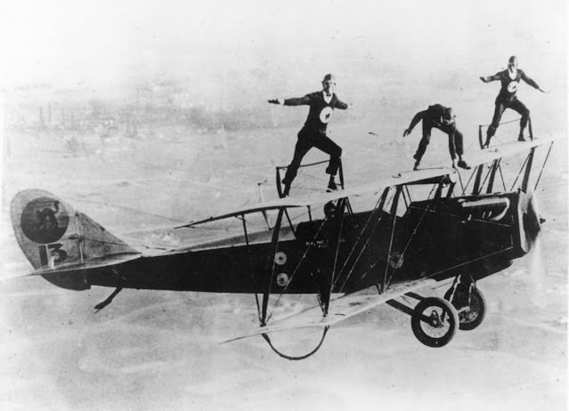 Bon MacDougall pilots while three Black Cats, from left to right, “Spider” Matlock, Al Johnson, and “Fronty” Nichols, balance on the upper wing. A smoke generator is under the nose of the airplane.