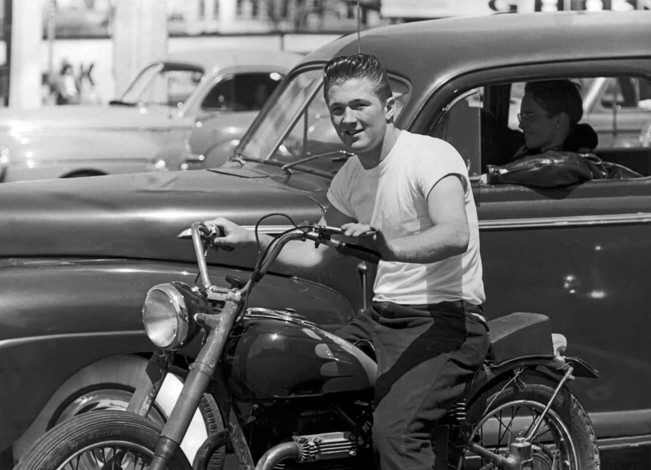 Young man on a motorcycle with a friend in a leather jacket in a car, San Francisco, California, circa 1955.
