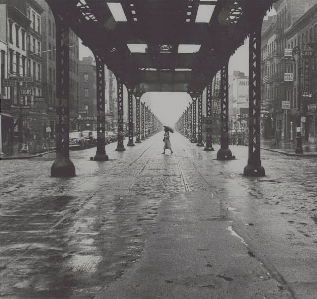 Woman with umbrella walking across New York City street, January 1956
