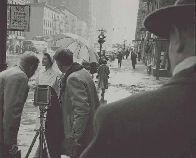 Woman being photographed in the rain on a street corner, 1954