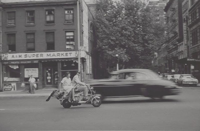 View of man and woman on motorized scooter, A&M Super Market in back, September 1957