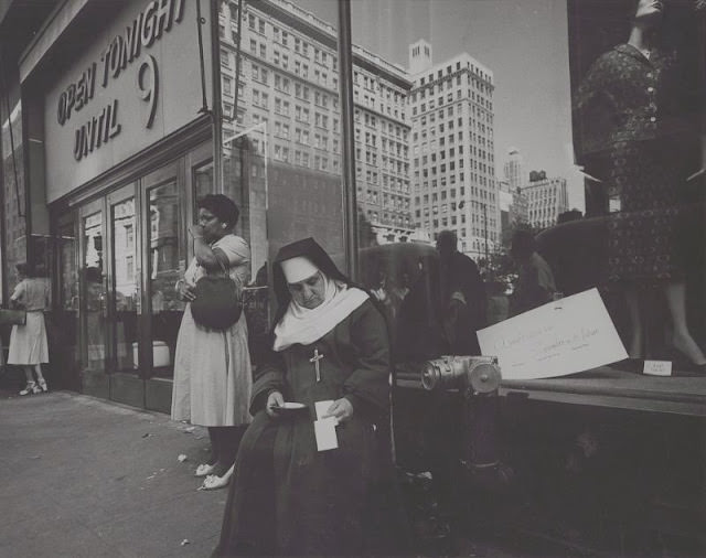 Nun sitting in front of a store window, August 1958