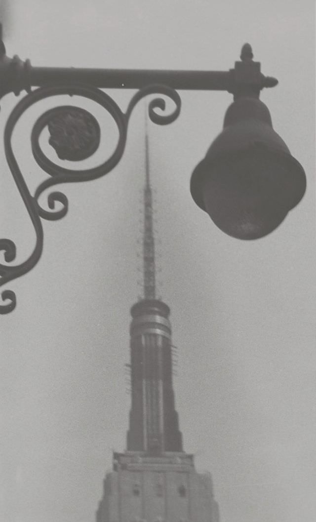 Detail view of upper portion of the Empire State Building seen through an ornate street lamp (foreground), Manhattan, New York City, New York, July 1959