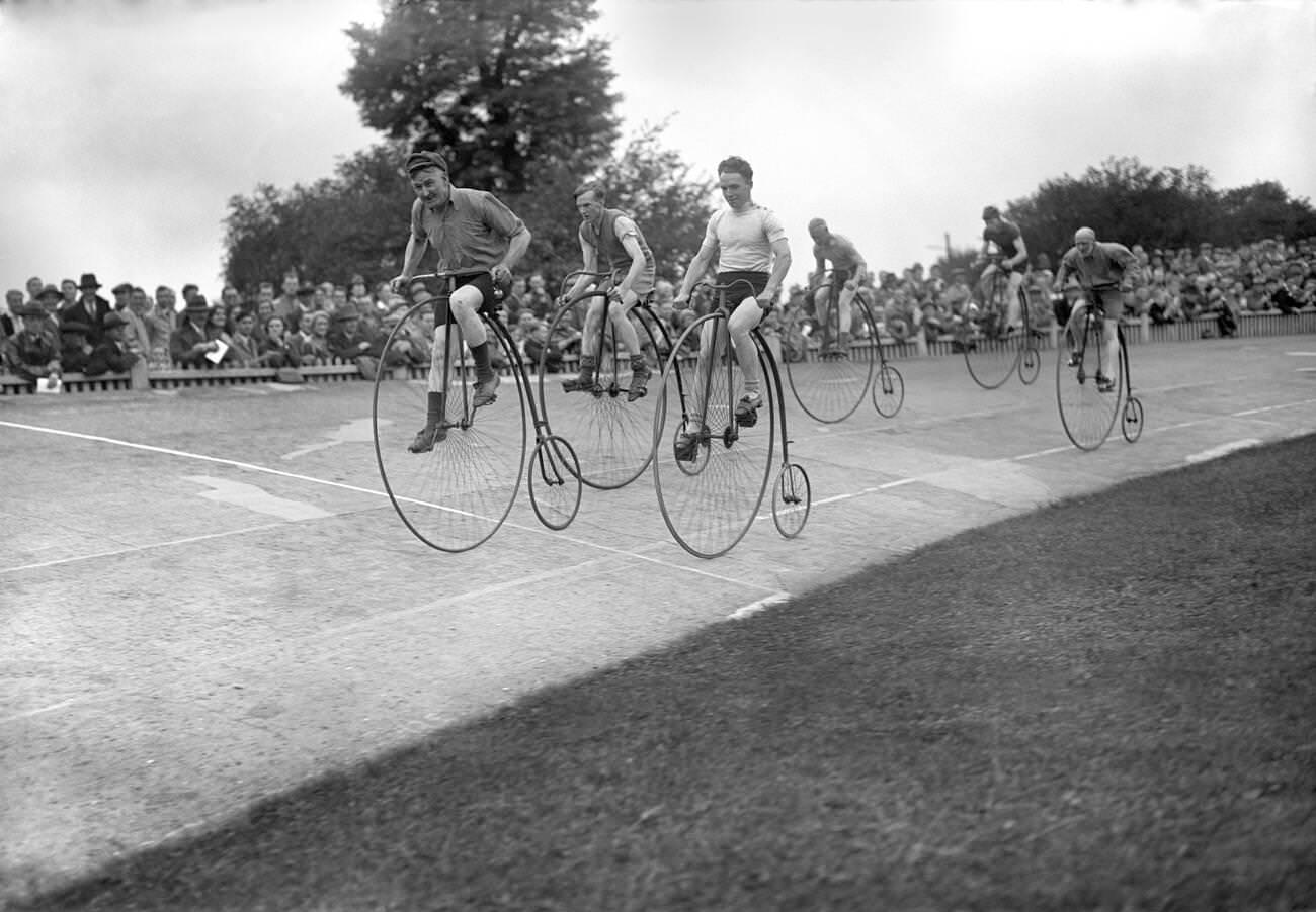 Penny farthing bicycle with a man riding beside another on a regular bicycle, 1930s.