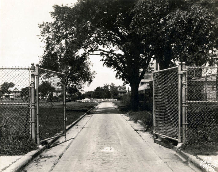 Steel double gate at entrance to distant dwellings, 1938.