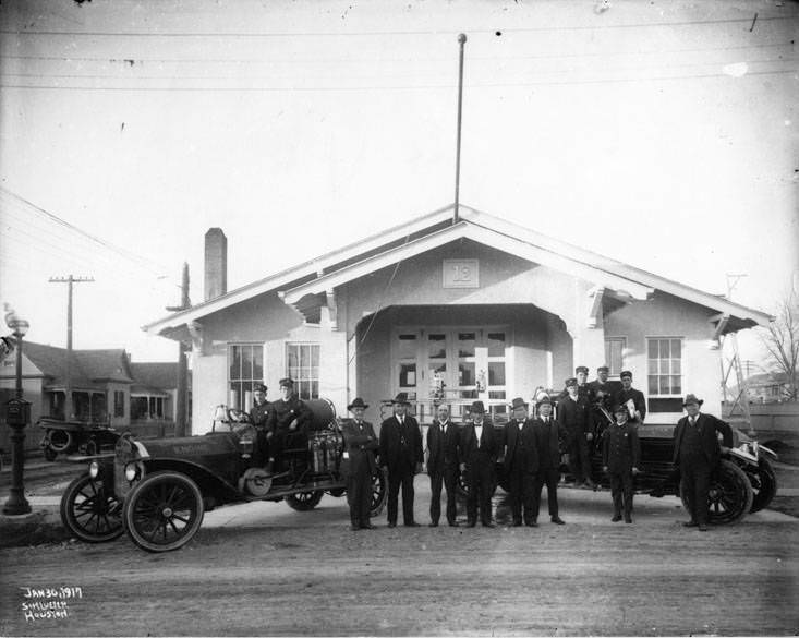 Men between two Houston firetrucks with steering wheels on the right, Fire Station No. 12 in the background, 1917.