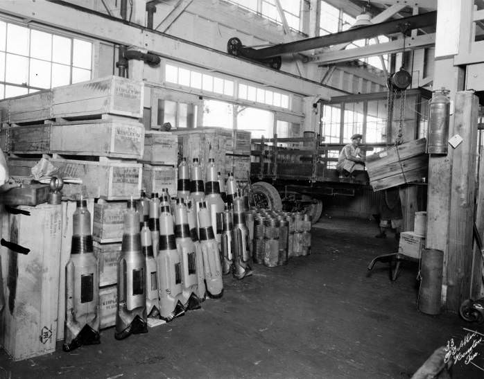 Man guiding Hughes Tool Co. products onto a truck with a crane, 1940s