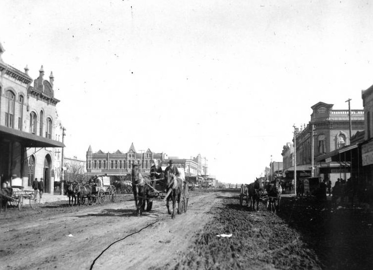 Street view in Hillsboro with shops and horse-drawn carriages, 1895