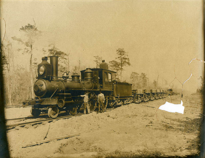 Two men beside railroad freight train engine, 1880s