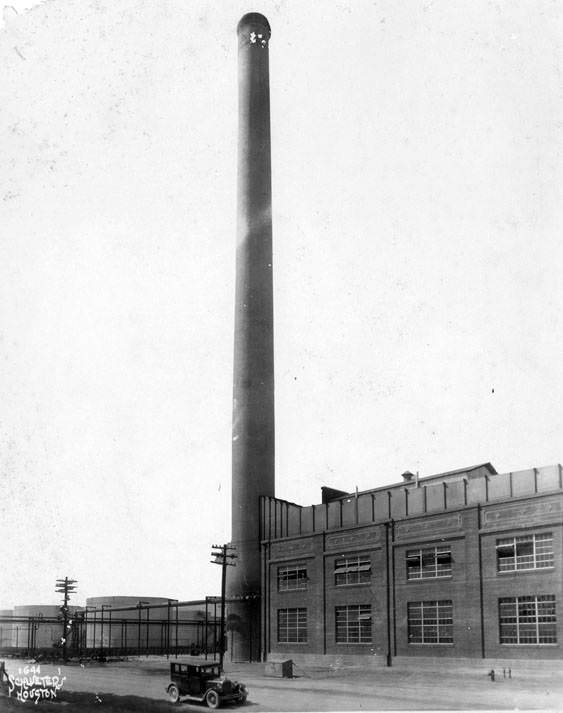 Smokestack between building and petroleum storage tanks, 1920s.