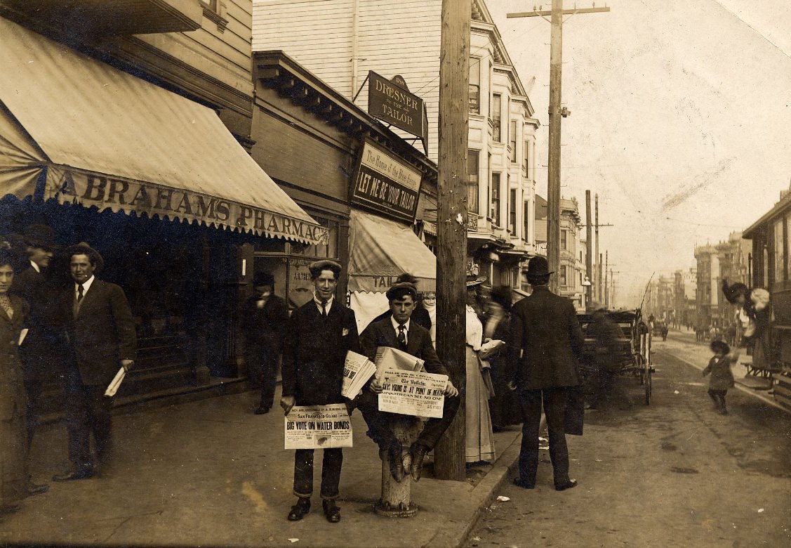 Pete Rielly and Eddie Campi selling newspapers in front of Abraham's Pharmacy, 1198 McAllister Street, at Fillmore, 1909