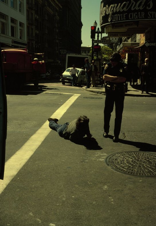Police officer looking at a person on the ground at O'Farrell Street and Powell Street, 1978.
