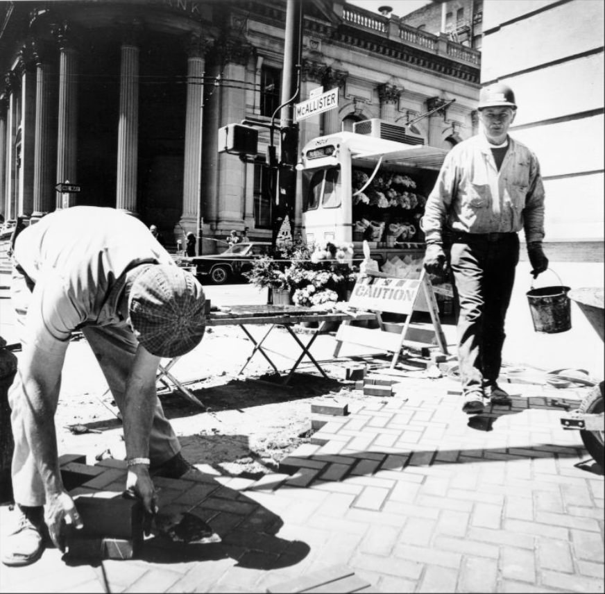 Men working on sidewalk widening project at Market and McAllister streets, 1970s.