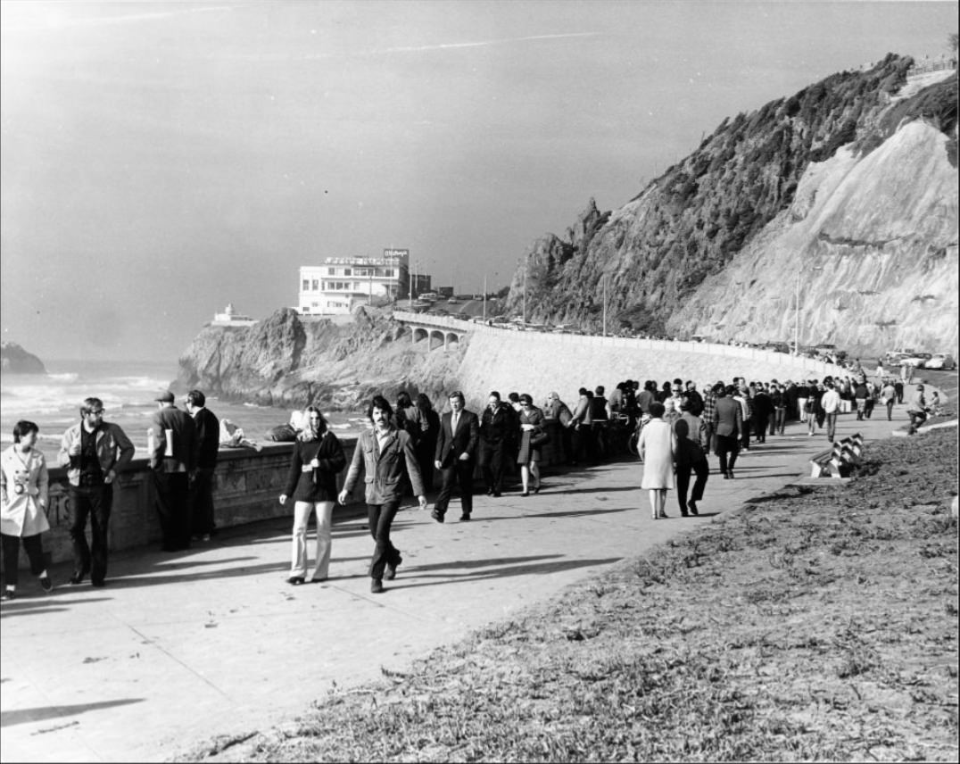 People walking along a sidewalk at Ocean Beach, near the Cliff House, 1971.